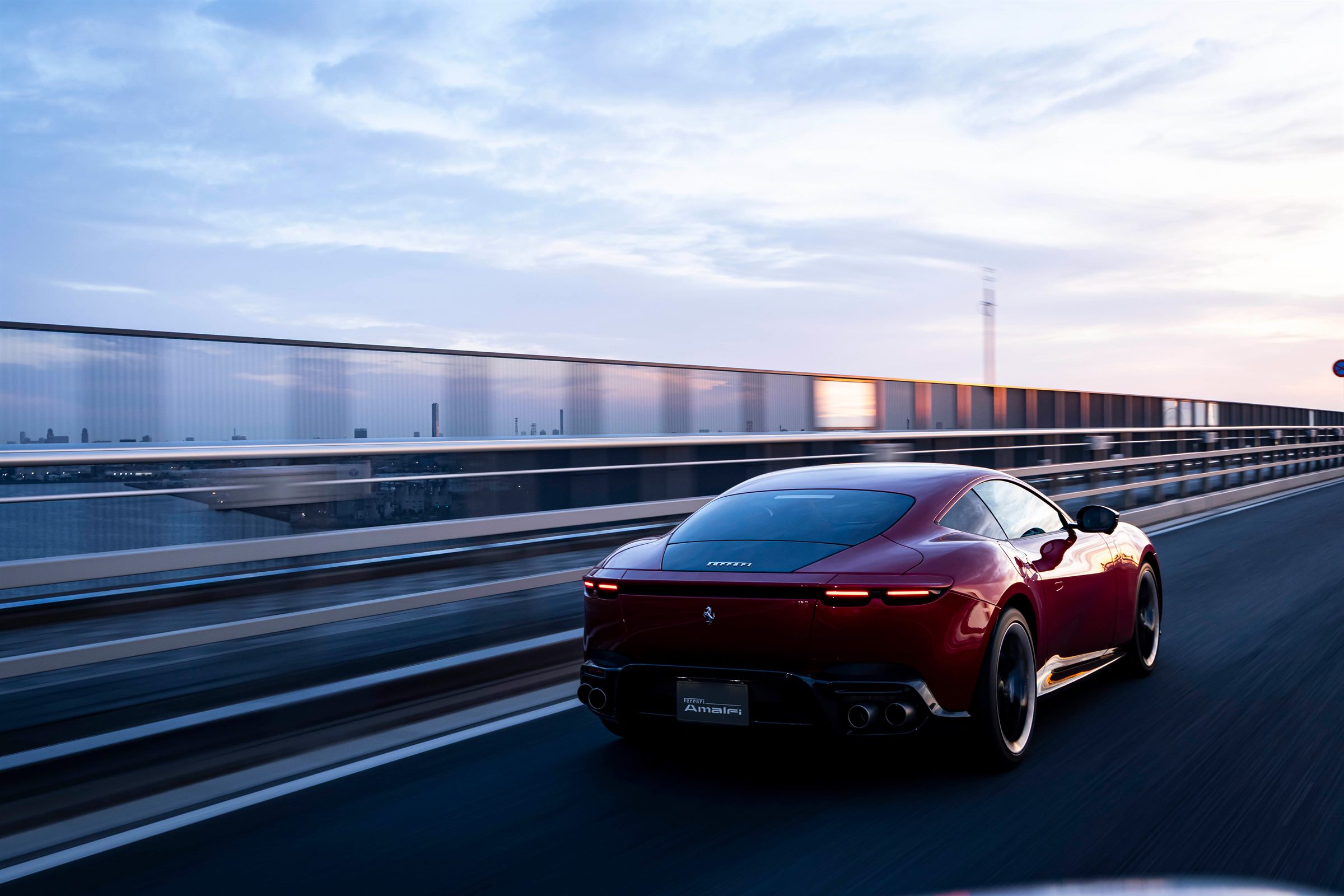 Ferrari Amalfi in Rosso Portofino on a coastal bridge at dusk